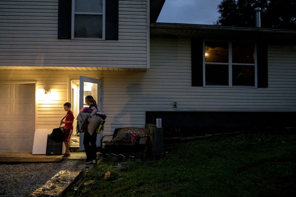 Third Place, Feature Picture Story - Jessica Phelps / Newark Advocate, “Nurses Go On Lockdown With Residents”At noon on March 12, two Licking County assisted living facilities closed their doors to the outside world for the sake of the 225 vulnerable residents within.They had been preparing for this day for three weeks, enlisting staff who would be willing to commit to 24-7 service for as long as the COVID-19 period of isolation would last; no one knew how long.The staff moved into any spare room, slept on air mattresses  in offices, and only saw loved ones through a phone screen for 65 days. The staff was committed and did not leave the assisted living facility for those long months. No one entered the buildings, no one left. And it worked. The staff kept the coronavirus from infecting patients while they were locked inside. Every photo was taken from outside the facilities, looking through the glass into the safe haven the nurses and aids created for the residents.Alisha Disbennett carries her luggage out to her car with help from her son Timmothy on July 31, 2020. Disbennett will be leaving her family for the next 30 days to be in 24 hour lockdown with the residents of the Inn at Chapel Grove where she works. The staff at the assisted living facility, along with its sister home, SharonBrooke spent 65 days in lockdown this spring to protect residents from contracting the coronavirus. As cases began to rise in Ohio the decision was made to again go into lockdown. So far no one has tested positive for the virus in either facility.